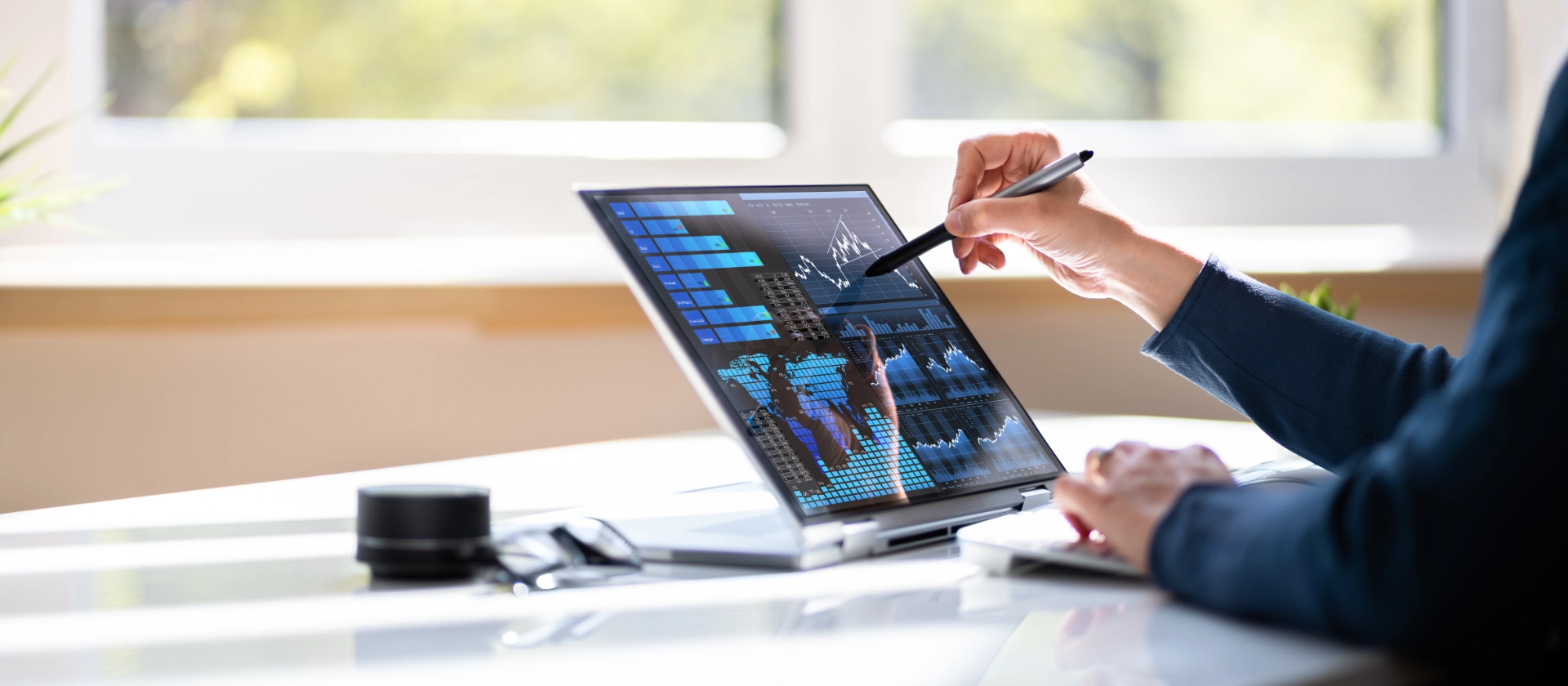 Person analysiert Finanzcharts auf einem Touchscreen-Laptop mit Stylus an einem modernen Schreibtisch.