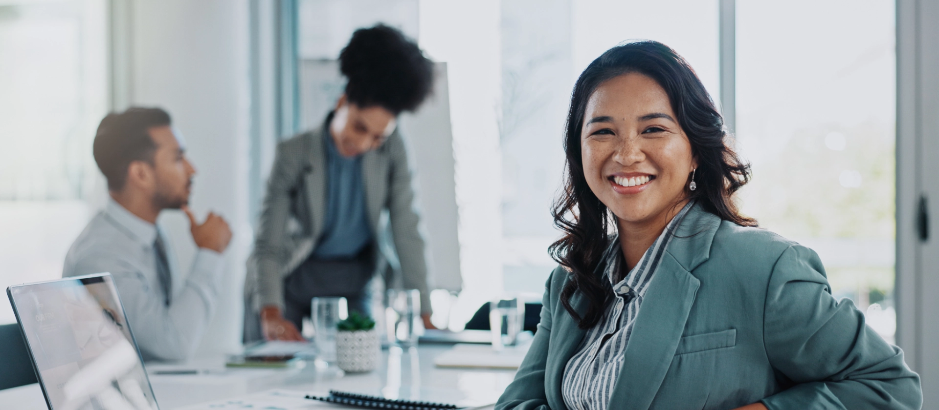 Lächelnde Frau in Büro mit Laptop zwei Kollegen im Hintergrund