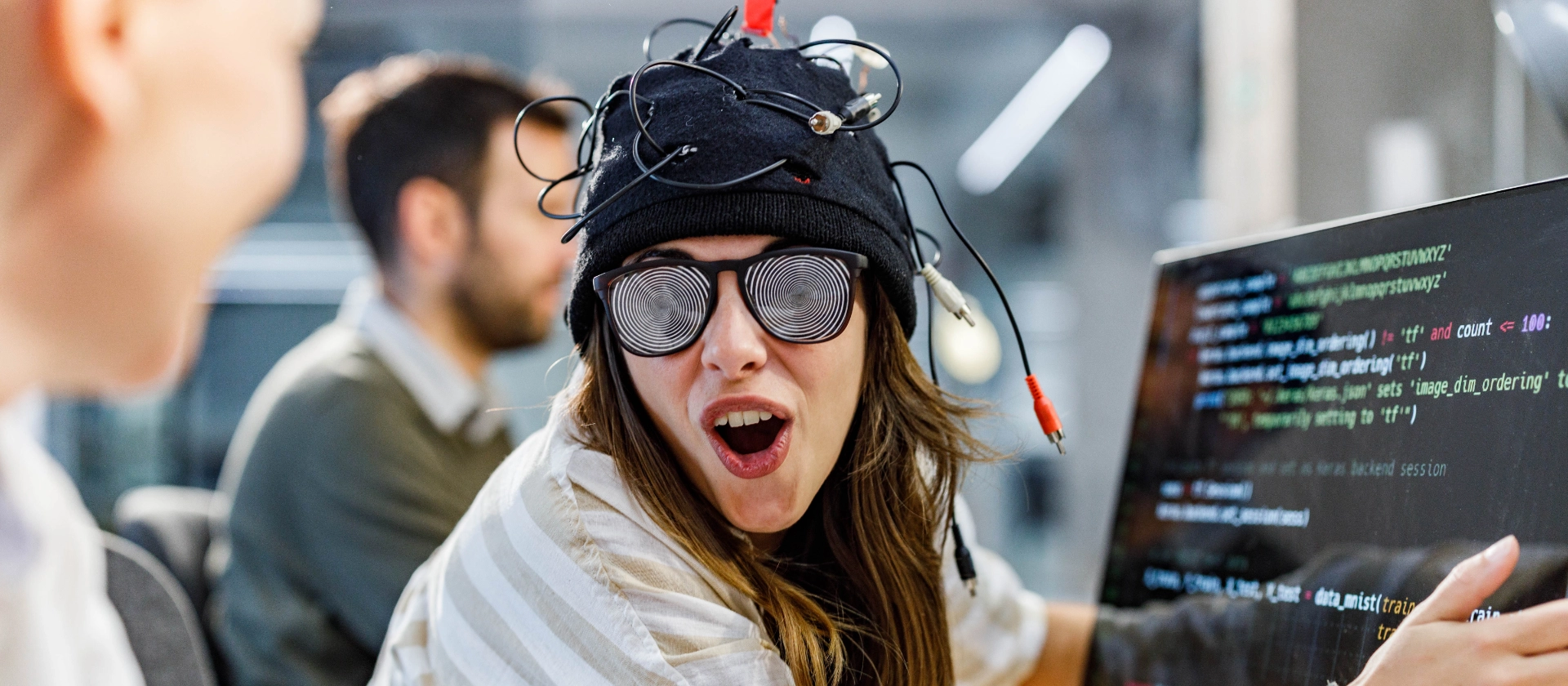 Spaßfoto einer jungen IT-Enthusiastin vor einem Bildschirm mit Code-Zeilen und einem futuristischem Helm