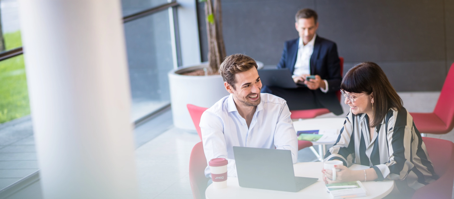 Männlicher und weiblicher Consultant im Foyer von msg in Ismaning bei einem schnellen Meeting an einem Tisch