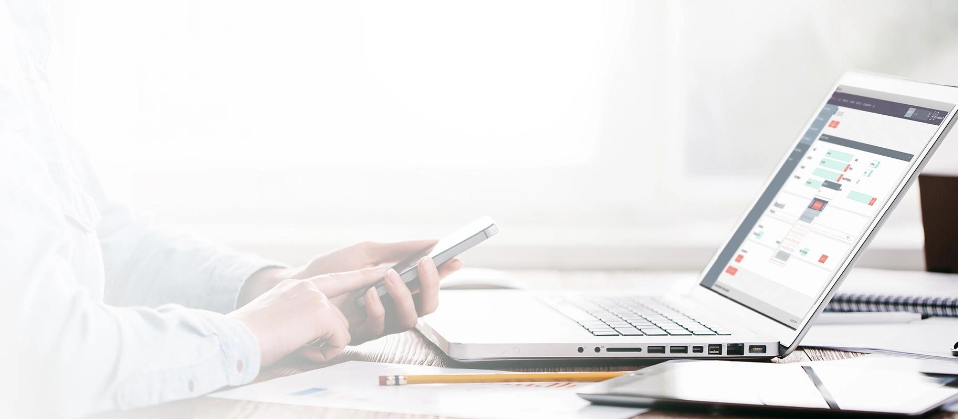 Person arbeitet an einem Schreibtisch mit Laptop und Smartphone; auf dem Laptop ist eine CRM-Software-Oberfläche geöffnet