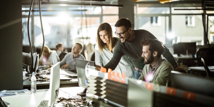 Drei Mitarbeitende der Corporate IT von msg betrachten lachend etwas auf einem Bildschirm