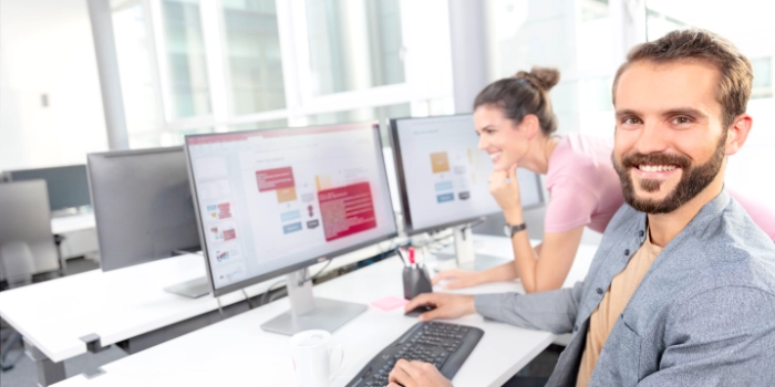 Zwei erfahrene Mitarbeitenden betrachten nebeneinander an ihren Arbeitsplätzen eine Powerpoint-Slide