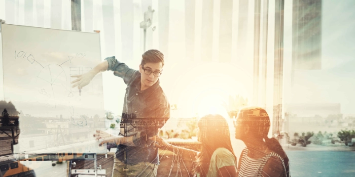 Ein Mitarbeiter aus dem Bereich Travel and Logistics präsentiert seinen Kolleginnen und Kollegen etwas an einem Whiteboard