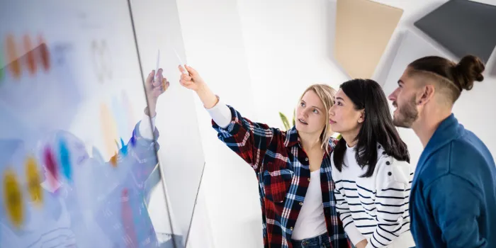 Gemischte Gruppe dreier Studierender, die konzentriert ein Kanban-Board am TV-Bildschirm betrachten