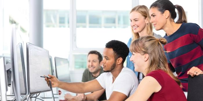 Eine gemischte Gruppe msg-Mitarbeitender kommt an einem Arbeitsplatz zusammen, um ein Arbeitsergebnis anzusehen