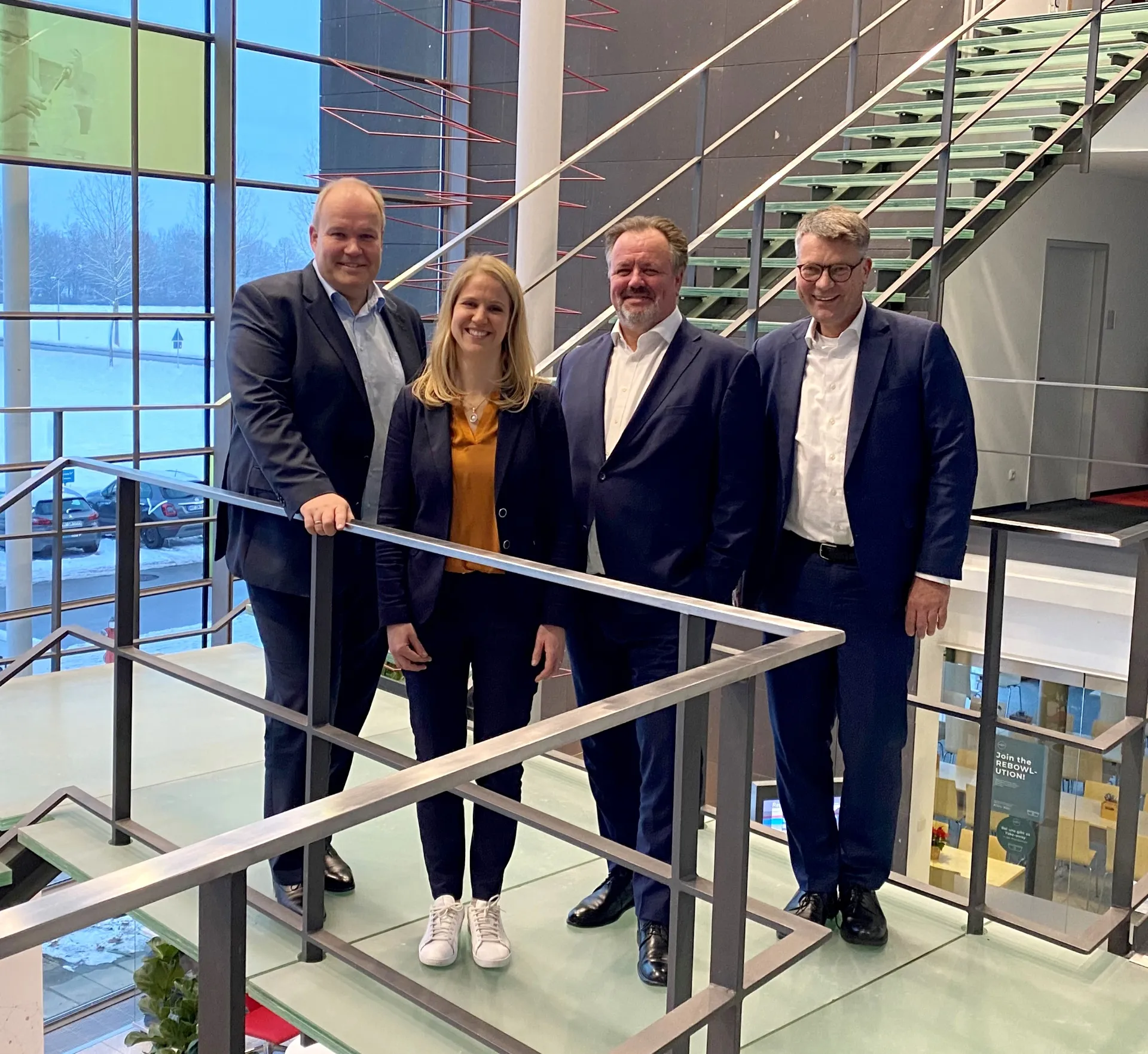 three men and one woman are smiling into the camera