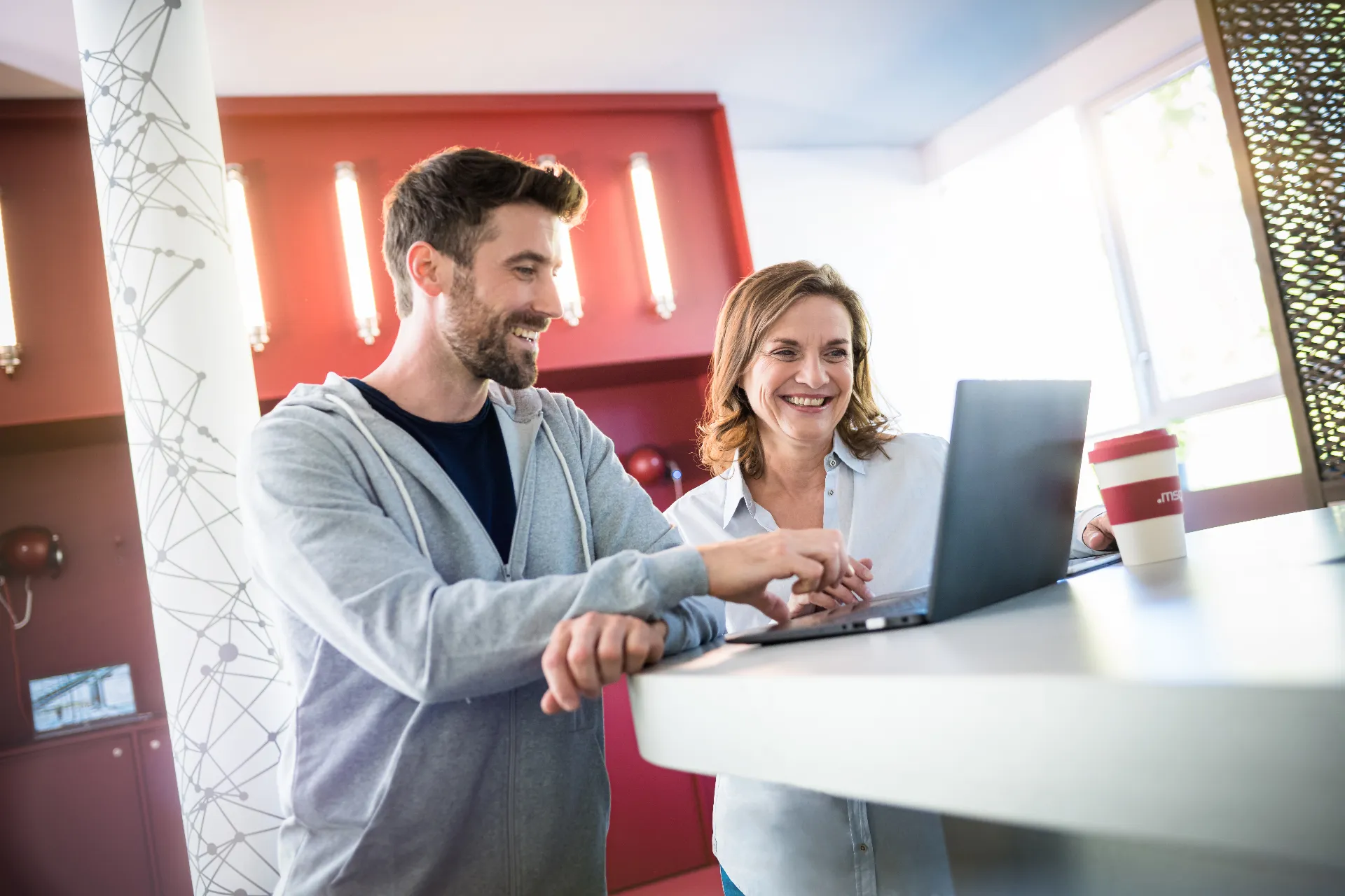 junger Entwickler zeigt erfahrener Kollegin Code am Laptop in der msg Service Lounge