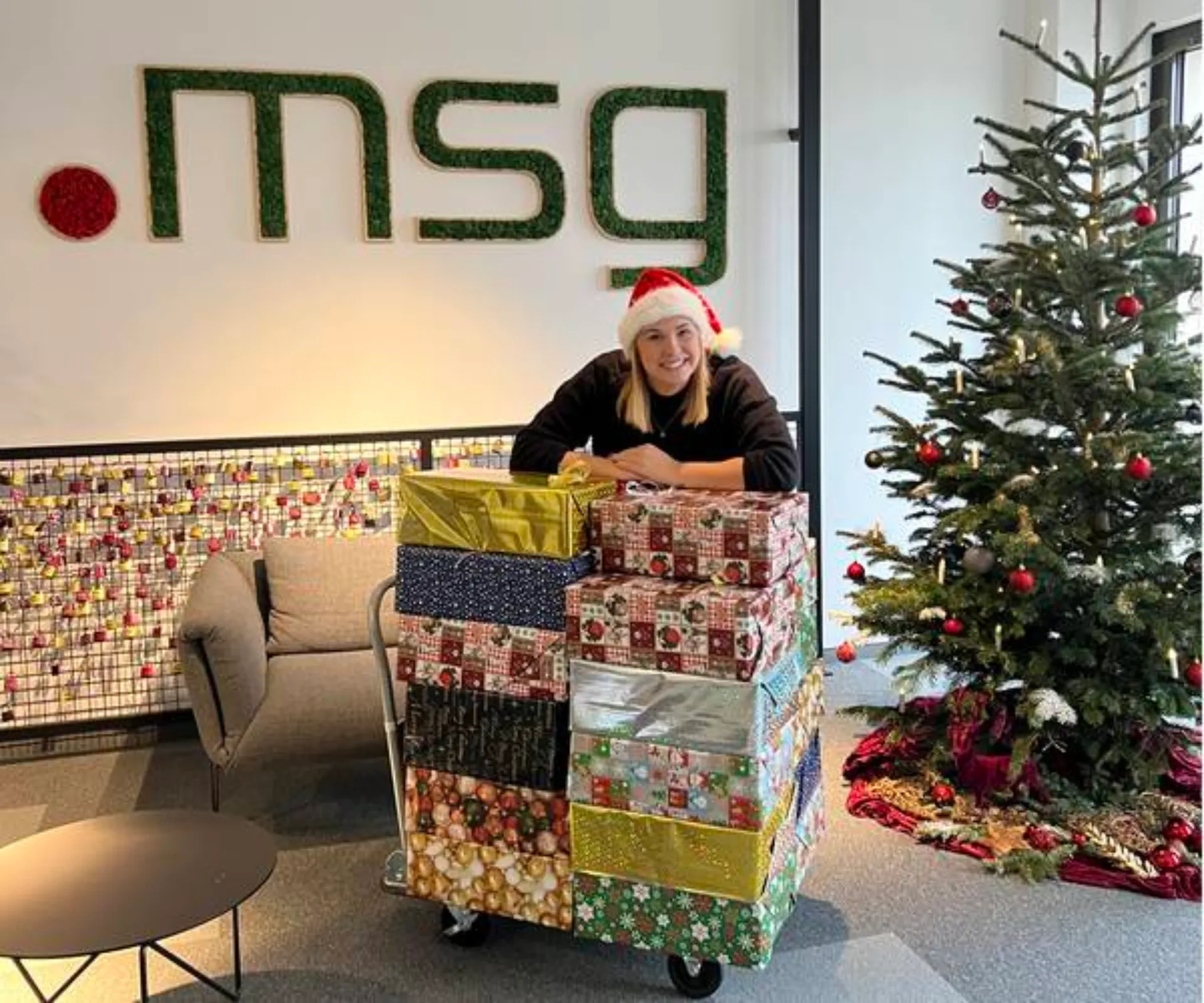 Mitarbeiterin beugt sich über einen Stapel mit Geschenken und lächelt.